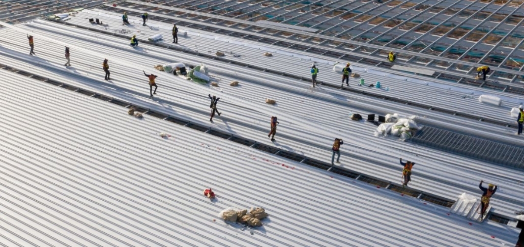 Workers installing metal panels on a commercial roof, focusing on structural repairs and decking replacement.