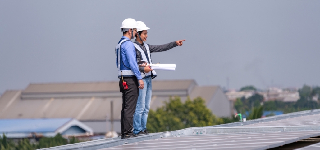 Two men on a rooftop, gesturing towards a specific area as part of the commercial roof replacement process.
