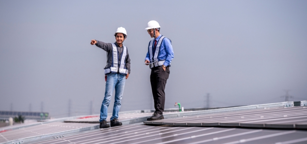 Two men conduct a final inspection of solar panels on a rooftop during a commercial roof replacement quality check.