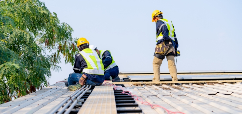 Three workers on a roof engaged in the removal of existing roofing, with a ladder for access during the commercial replacement.