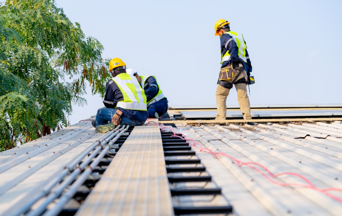 Three workers on a roof, focused on installing a metal roof for an industrial roofing company serving warehouses and schools.