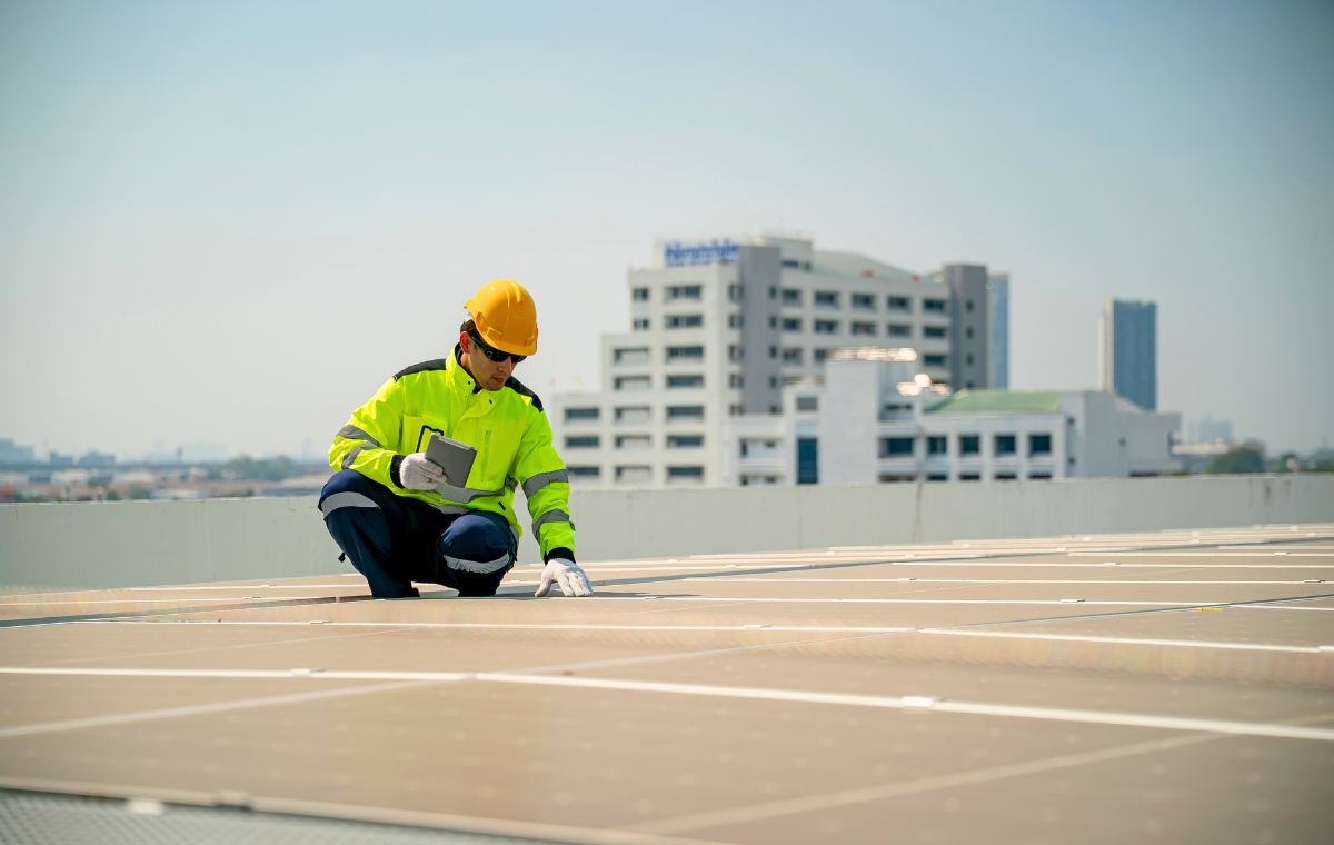 A worker in a yellow safety vest and hard hat stands on a building's flat roof, representing commercial roofing services.