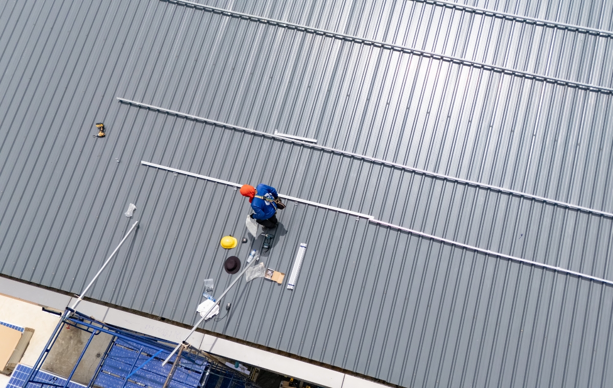 Aerial perspective of a worker on a commercial roof, engaged in repair work with safety gear and equipment visible.