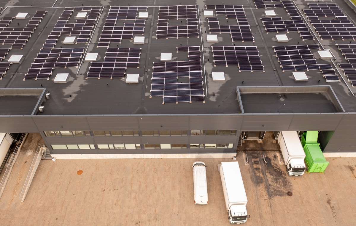 Aerial perspective of a spacious warehouse with solar panels on the roof, showcasing eco-friendly business practices.