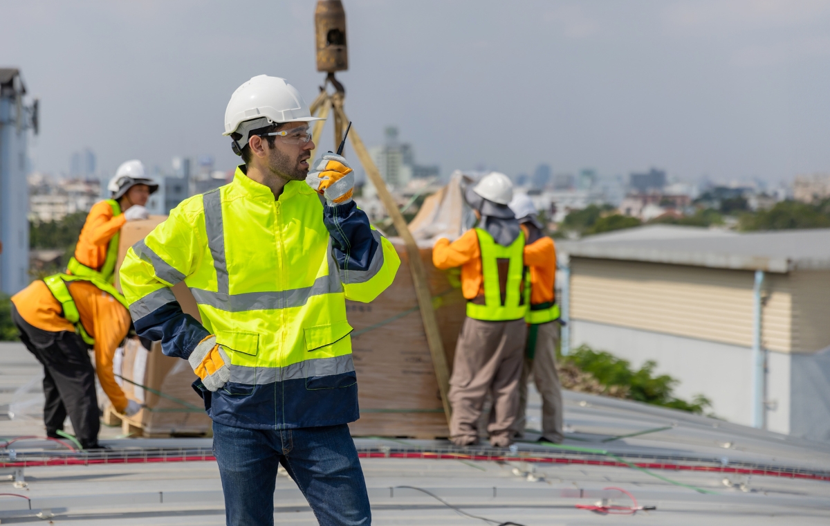 A man in a safety vest stands on a roof, overseeing the installation of a new roof for a business.