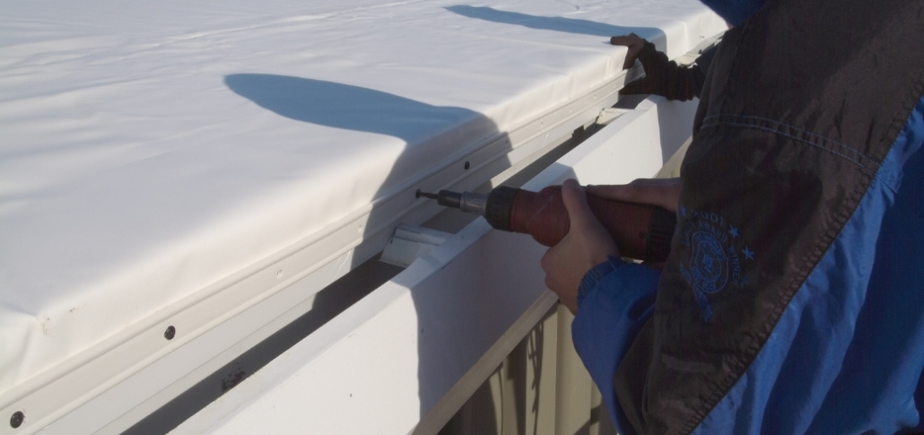 A man drills to install edge metal on a TPO roof cover, ensuring a secure fit for the roofing material.