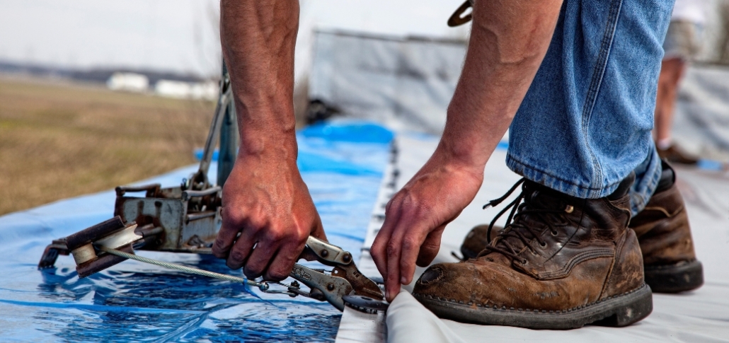A person securing the membrane with a tool during a TPO roof installation process.