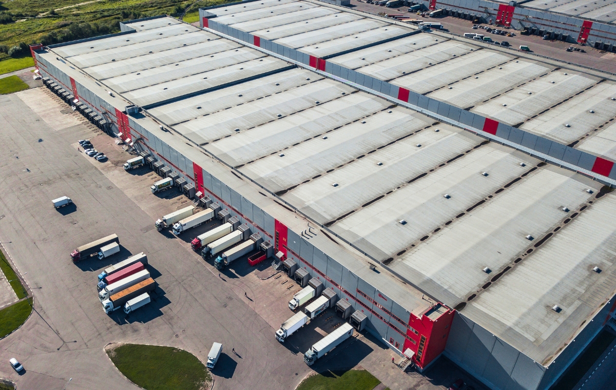 Aerial view of a large warehouse with trucks parked in front, showcasing the warehouse roofing and surrounding area.