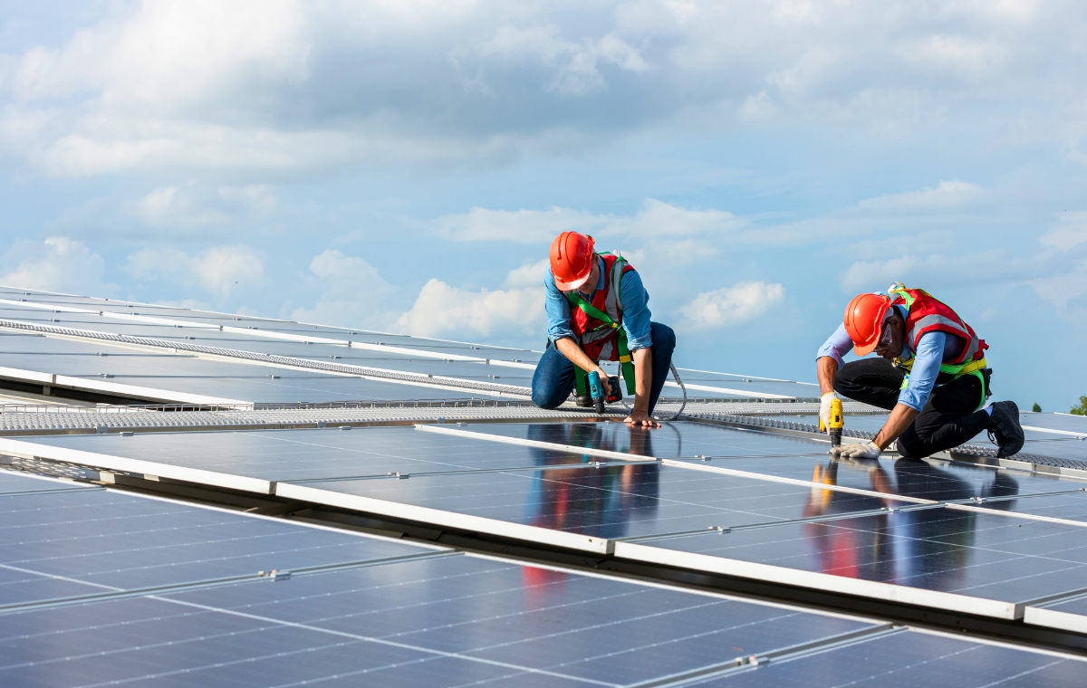 Two workers in orange vests are installing solar panels on a commercial roof in Hartford, Connecticut.