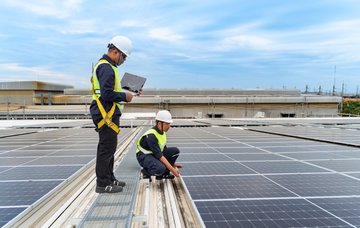 Two commercial roofers in safety vests on a rooftop solar panel installation in Hartford, CT.