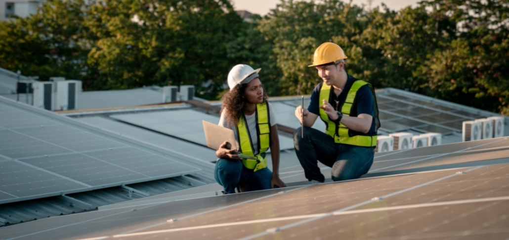 Two workers in hard hats inspecting solar panels on a rooftop, addressing commercial roof problems and diagnostics.
