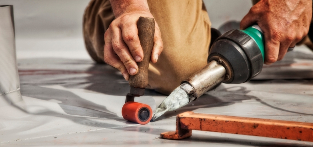 A man heat-weld a patch on the roof, illustrating techniques for addressing commercial roof problems permanently.