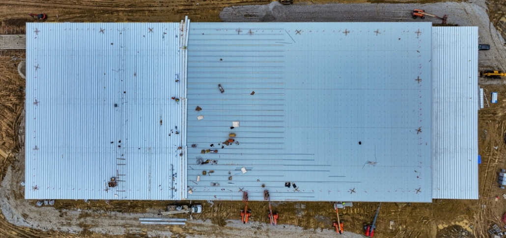 Aerial view of a warehouse where construction workers evaluate roofing materials and coatings for commercial repairs.