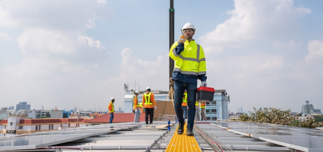 A man in a safety vest stands on a roof, inspecting solar panels, promoting professional roof repair services.