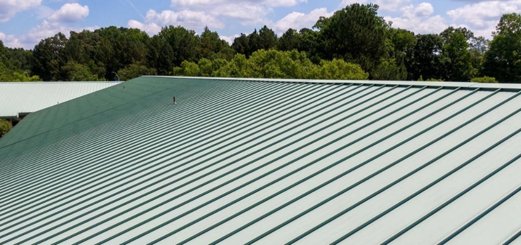 A green metal roof contrasted with a blue sky, illustrating commercial roofing solutions for industrial buildings.