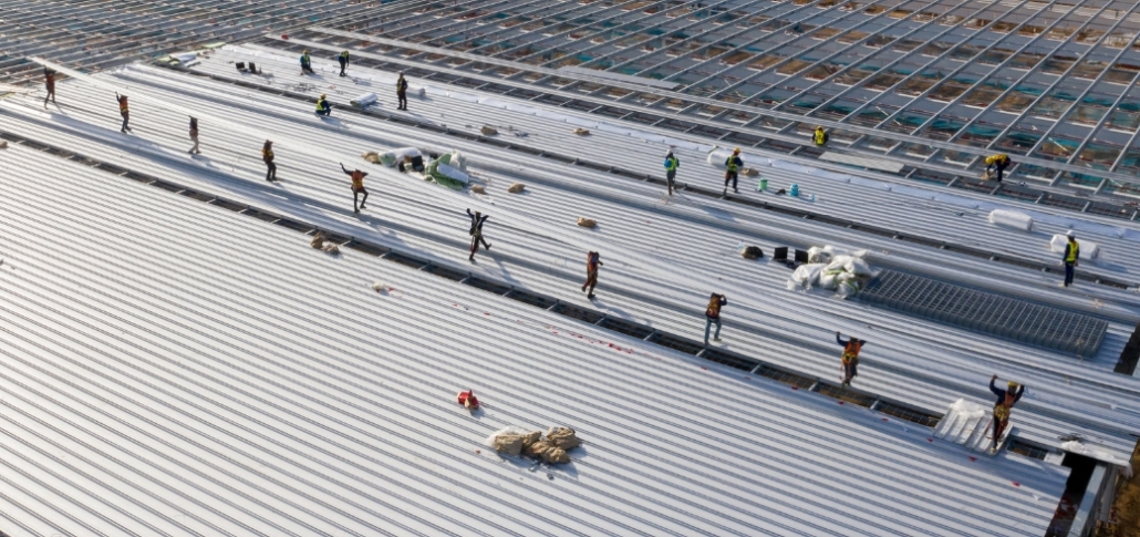 Workers installing a commercial roof on an industrial building, showcasing a professional roofing process.