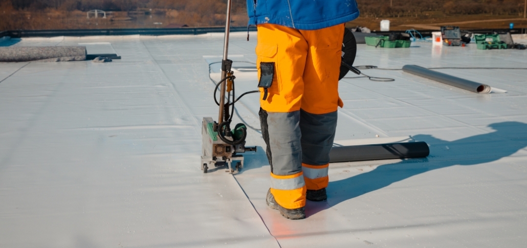 A man wearing orange pants stands on a roof, engaged in EPDM roof installation, emphasizing leak prevention and warranty protection.